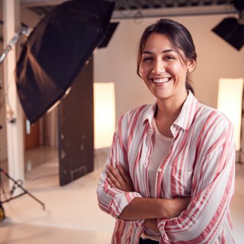 Portrait Of Smiling Female Photographer Standing In Studio With Lighting Equipment